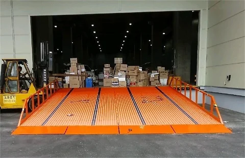 倉庫床に接続された幅広のオレンジ色ドックランプの実物